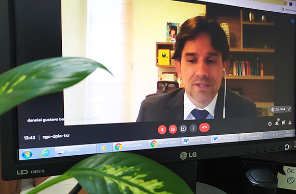 Fotografia do monitor de um computador com a imagem da videochamda. Aparecem na foto juiz Danniel Bomfim e no canto inferior esquerdo folhas de uma planta