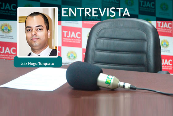 Foto do microfone e uma folha de papel sobre uma mesa, atrás uma cadeira e um banner com a logomarca do TJAC e por cima da imagem um quadradinho com a foto do juiz Hugo Torquato e ao lado a palavra entrevista