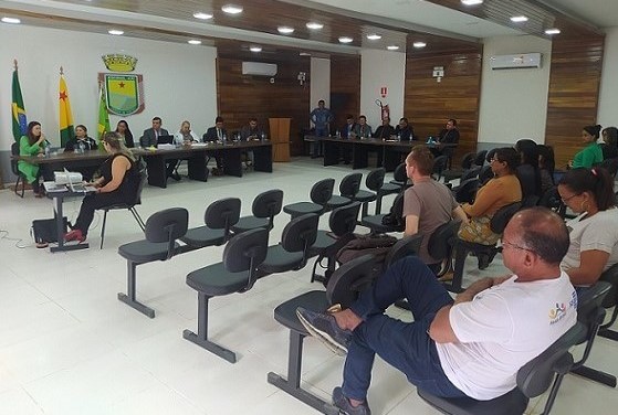 Foto da plenária de Assis Brasil, com pessoas na platéia e ao fundo a bancada dos vereadores e vereadoras