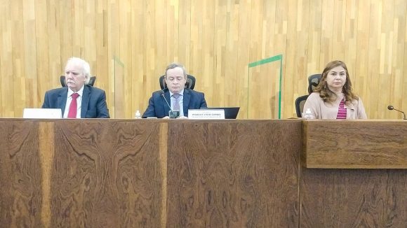 Três pessoas sentadas em uma bancada olhando para frente