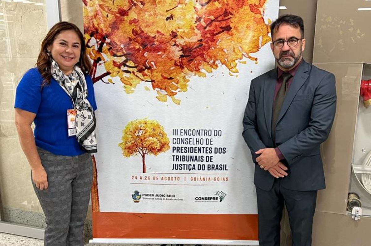 Foto da desembargadora Waldirene e do juiz Leandro posando ao lado do banner do evento