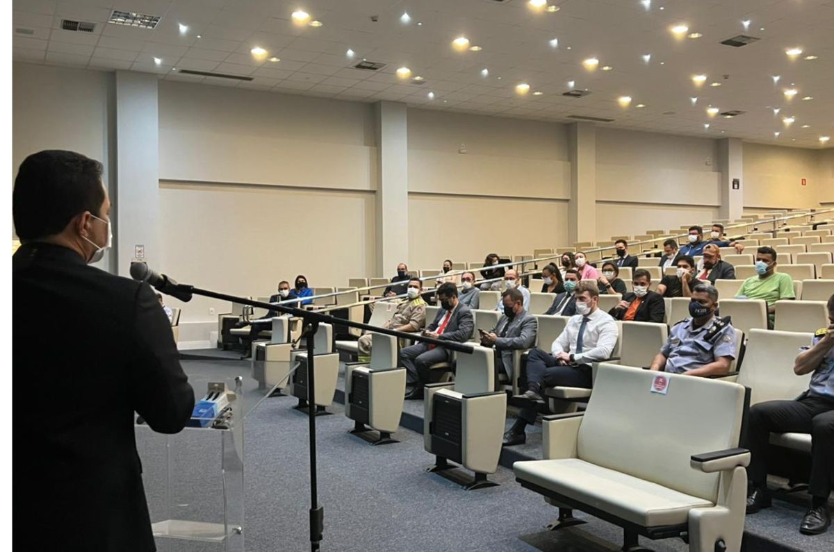 Imagem do juiz eleitoral falando e a sua frente a plateia sentada em cadeiras brancas