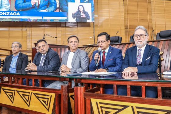 Foto do deputado Luiz Gonzaga discursando. Ao lado direito dele, o desembargador Luís Camolez; à esquerda, o senador Márcio Bittar.
