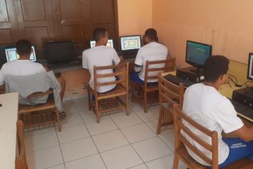 Foto de socioeducandos estudando. Na imagem aparecem quatro, todos vestidos com blusas brancas e shorts azuis.