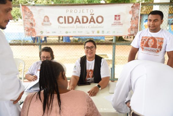 A imagem mostrar duas pessoas e um homem em atendimento aos casais que estão a participar do "Projeto Cidadão". As mulheres vestem a blusa com identificação do projeto uma esta de blazer preto sem manga preto, o homem vestir a camisa do projeto também. O momento da atmosfera é de alegria e tranquilidade.
