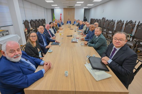 Na imagem, há vinte e seis pessoas ao todo, todas sentadas à mesa, com as mãos sobre a mesa em posição para tirar uma foto, captada por câmera profissional ou celular. A imagem transmite a atmosfera de alegria e concentração dos juízes e juízas ali presentes.