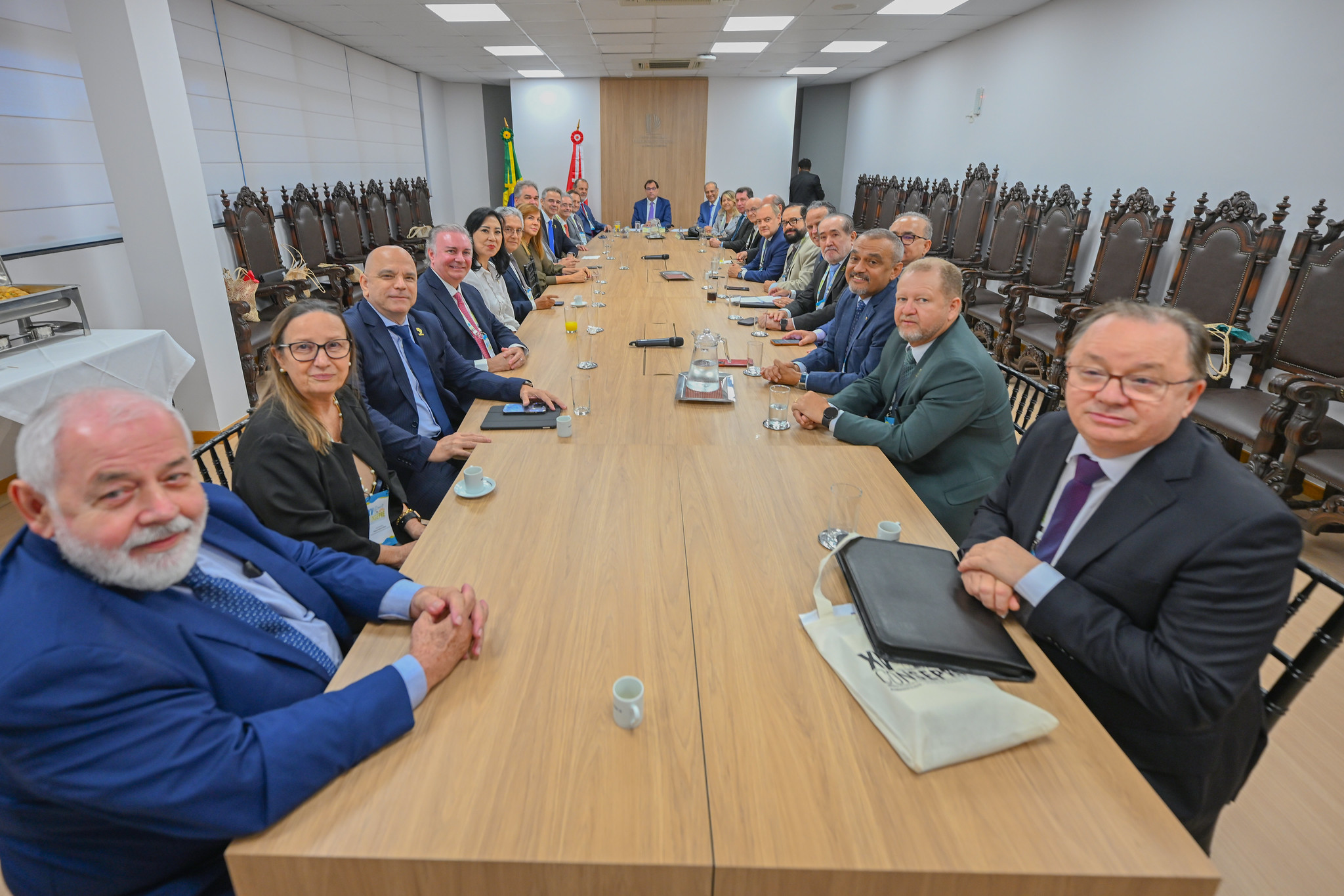 Na imagem, há vinte e seis pessoas ao todo, todas sentadas à mesa, com as mãos sobre a mesa em posição para tirar uma foto, captada por câmera profissional ou celular. A imagem transmite a atmosfera de alegria e concentração dos juízes e juízas ali presentes.