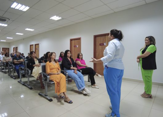 Na imagem, é possível ver a enfermeira e a psicóloga de frente para as pessoas sentadas, assistindo à palestra. A imagem passar a sensação de compreensão do assunto tratado sobre câncer no colo uterino e retal ali.