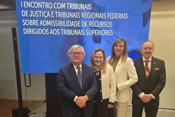 A imagem mostra quatro pessoas posando para uma foto diante de um painel digital, em um ambiente formal e institucional. O painel ao fundo exibe o título do evento: "I Encontro com Tribunais de Justiça e Tribunais Regionais Federais sobre Admissibilidade de Recursos Dirigidos aos Tribunais Superiores". Trata-se claramente de um evento jurídico de alto nível, possivelmente realizado em Brasília, voltado à discussão de temas relacionados ao funcionamento e à tramitação de recursos no sistema judiciário brasileiro. As quatro pessoas na imagem estão bem vestidas, com roupas formais: Os dois homens usam ternos escuros, gravatas e camisas claras. As duas mulheres estão com trajes sociais elegantes — uma com um conjunto preto e blazer claro, e a outra com blazer branco. Todos sorriem e estão dispostos lado a lado em frente ao painel. O cenário reforça a natureza solene do encontro, indicando que são provavelmente magistrados, desembargadores ou servidores de alto escalão da Justiça brasileira.