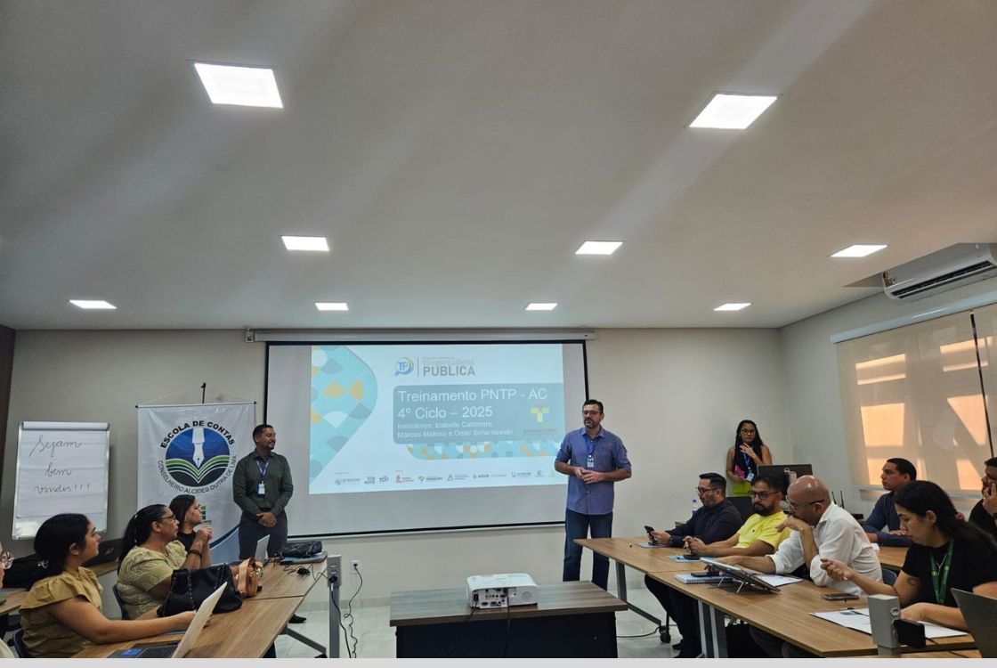 A imagem mostra um ambiente de treinamento ou capacitação profissional, realizado em uma sala de reuniões moderna e bem iluminada. No centro, um projetor exibe na tela a apresentação do evento intitulado: "Treinamento PNTP – AC 4º Ciclo – 2025" Com os nomes dos instrutores: Izabelle Calegario, Marcos Matoso e Oscar Szwarcowski. O evento é promovido pela Plataforma Pública, em parceria com diversas instituições, cujos logotipos aparecem na parte inferior do slide. Do lado esquerdo da tela há um banner com o emblema da Escola de Contas Conselheiro Alcides Dutra, vinculada ao Tribunal de Contas do Estado do Acre. Na sala, cerca de quinze participantes, entre homens e mulheres, estão sentados em torno de mesas em formato de U, alguns atentos à apresentação, outros interagindo com celulares, tablets ou notebooks. Dois homens estão de pé na frente da sala, conduzindo a abertura ou explicação inicial do treinamento. Uma terceira pessoa, uma mulher, também está de pé próxima ao fundo da sala. À esquerda, um quadro com a frase escrita à mão: "Sejam bem-vindos!!!" reforça o caráter acolhedor da atividade. A atmosfera é de formalidade moderada, típica de eventos educacionais ou de capacitação para servidores públicos, com foco em profissionalização, troca de conhecimentos e atualização de práticas institucionais.