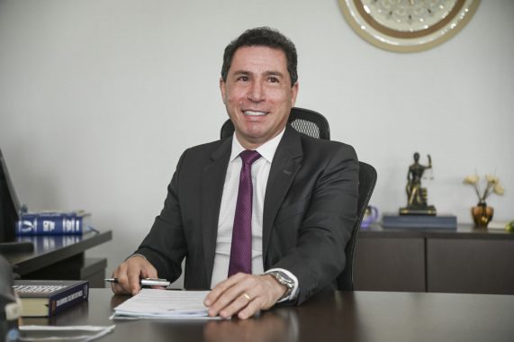 Na imagem o desembargador, presidente do TJAC, Laudivon Nogueira, ele tem a cor de pele branca, cabelo social preto, usa terno preto, camisa social branca e gravata violeta, ele esta sorrindo para foto.