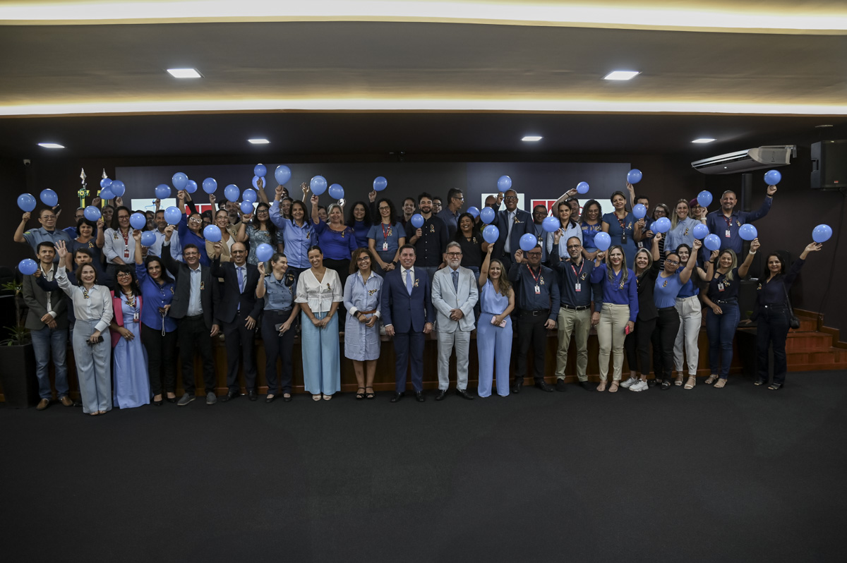 A imagem mostra um grande grupo de pessoas reunidas em um auditório, posando para uma foto coletiva. A maioria das pessoas está vestida em tons de azul e segurando balões azuis, o que sugere que o evento possa estar relacionado a uma campanha de conscientização, como o Novembro Azul, que promove a prevenção do câncer de próstata. No fundo, aparecem os logotipos da ESJUD (Escola do Poder Judiciário do Estado do Acre) e do Poder Judiciário do Estado do Acre, indicando que o evento está sendo realizado por essa instituição. As pessoas estão sorrindo e demonstram um clima de união, celebração e engajamento institucional. A imagem transmite um ambiente acolhedor, colaborativo e de apoio a uma causa comum.