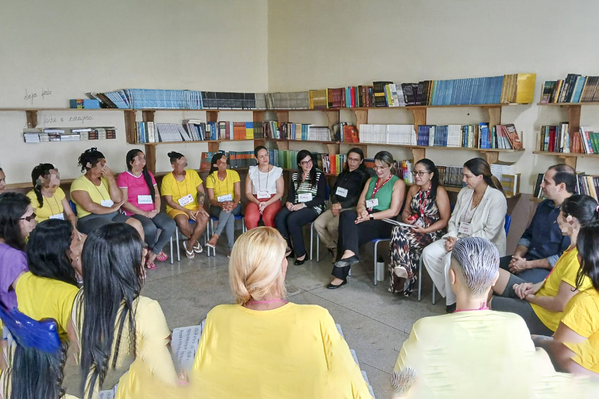 A imagem mostra uma roda de conversa realizada em um ambiente simples e acolhedor, possivelmente uma biblioteca ou sala de leitura. A atividade parece ser voltada à escuta, diálogo e reflexão, com participação de diversas pessoas — algumas provavelmente privadas de liberdade, outras facilitadoras ou representantes de instituições. O cenário parece fazer parte de uma ação social, projeto de ressocialização ou atividade de justiça restaurativa, com foco na valorização da palavra, do afeto e do aprendizado. A presença de facilitadores externos indica uma possível parceria entre instituições de justiça, educação e assistência social.