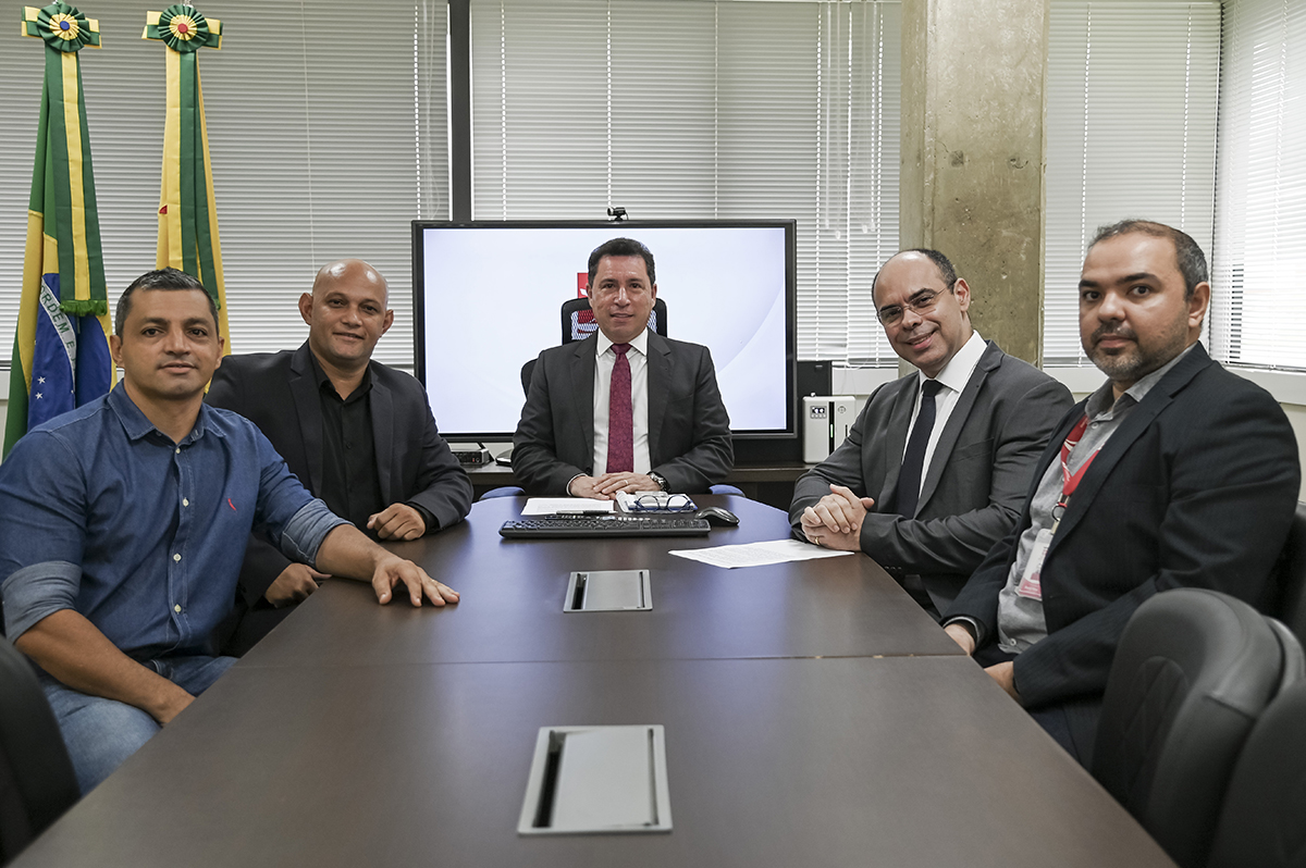 Na imagem, cinco homens com trajes formais estão olhando em direção a camêra após provavelmente um reunião